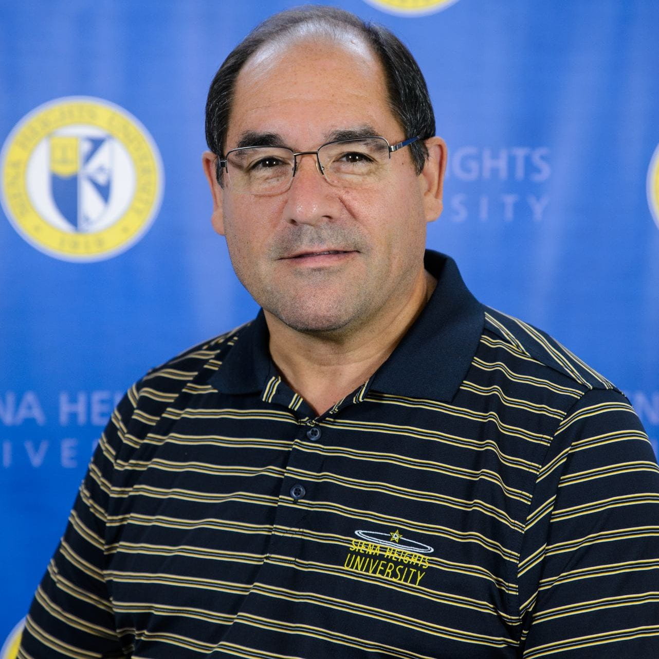 A photograph of Joseph Costello with Siena Heights backdrop
